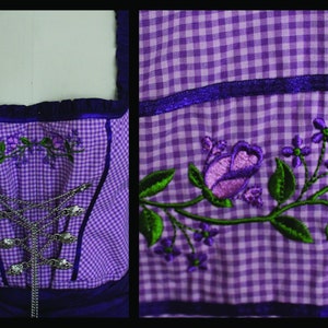 May include: A purple and white checkered bodice with embroidered floral details. The bodice features a silver chain closure and is trimmed with dark purple fabric. The embroidery includes purple roses and green leaves, creating a traditional aesthetic.