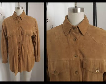 May include: A brown suede shirt with a button-down collar and long sleeves. The shirt has two chest pockets and a single button closure.