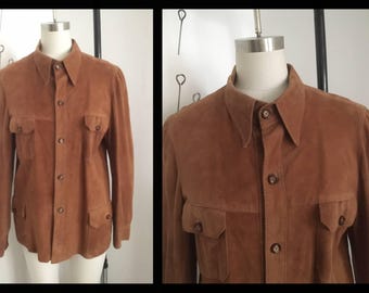 May include: A brown suede shirt with a button-down collar and long sleeves. The shirt has two flap pockets on the chest and a button closure.