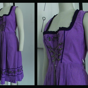 May include: A sleeveless purple gingham dress with a square neckline and a fitted bodice. The bodice features a decorative metal closure and embroidered floral accents. The hemline is adorned with embroidered floral details.