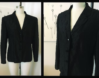 May include: A black blazer with a textured fabric and a button closure. The blazer has a classic style and is adorned with small black beads.