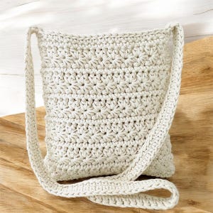 May include: A cream-colored crocheted crossbody bag with a long strap. The bag is made with a simple stitch pattern and has a slightly textured surface.