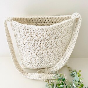May include: A white crocheted tote bag with a long strap. The bag has a simple, textured design.