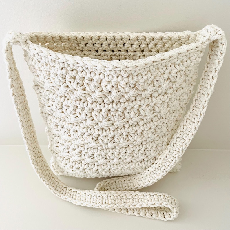 May include: A white crocheted crossbody bag with a long strap. The bag is made with a textured stitch pattern.