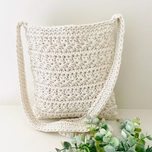 May include: A crocheted cream-colored crossbody bag with a long strap. The bag has a textured, star-shaped pattern.
