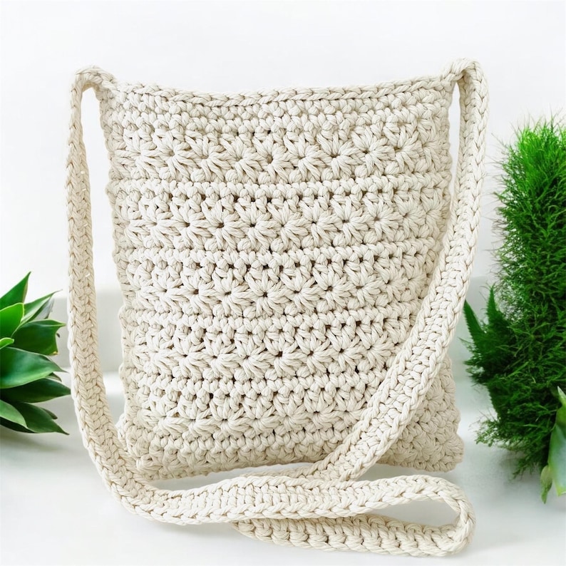 May include: A cream-colored crocheted crossbody bag with a long strap. The bag is made of a thick, textured yarn and has a simple, elegant design.
