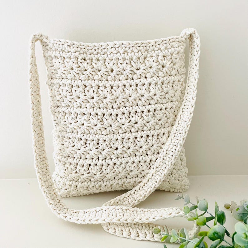 May include: A white crocheted crossbody bag with a long strap. The bag has a star-shaped stitch pattern.