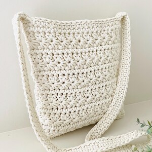 May include: A white crocheted shoulder bag with a long strap. The bag has a simple, textured design.