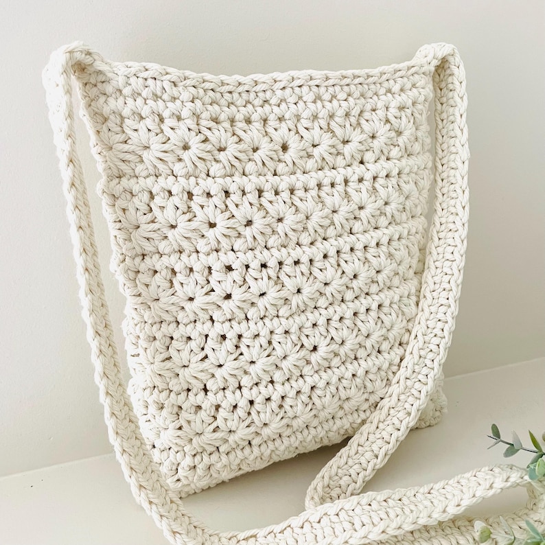 May include: A white crocheted shoulder bag with a long strap. The bag has a simple, textured design.