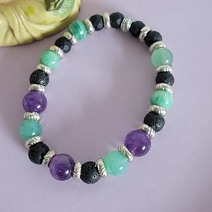 May include: A bracelet made with amethyst, green aventurine, and black lava rock beads. The beads are separated by silver spacers.