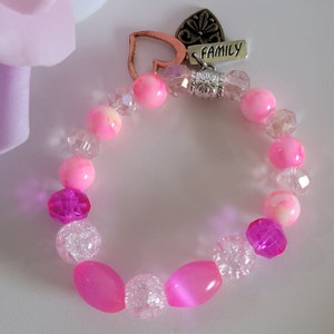 Könnte beinhalten: Rosa und klares Perlenarmband mit einem silbernen Anhänger, auf dem "FAMILY" steht.