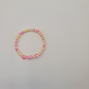 Könnte beinhalten: Ein rosa und gelbes Perlenarmband mit perlmuttartigem Finish.