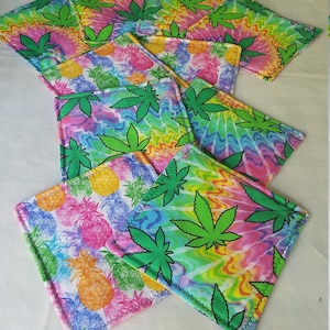 May include: A set of colorful coasters featuring a tie-dye pattern with green marijuana leaves and pineapple designs.