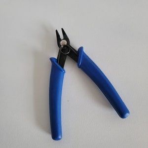 May include: Blue handled wire cutters with a black metal head. The cutters have a spring-loaded handle.