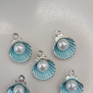May include: Five silver charms shaped like seashells with a pearl in the center. The shells are a light blue color.