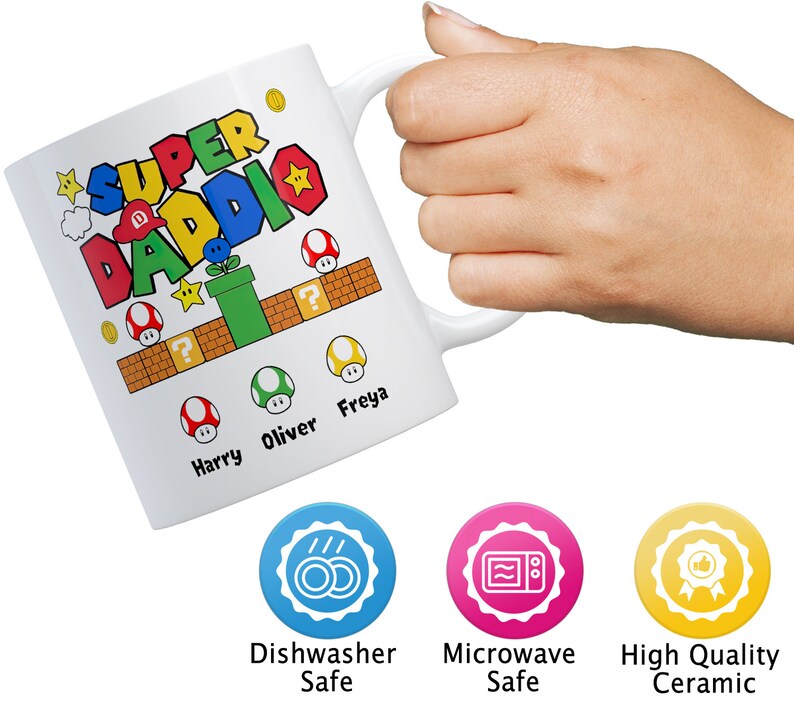 May include: White ceramic mug with a colorful Super Daddie design featuring a video game theme. The mug has the names Harry, Oliver, and Freya printed on it. The mug is dishwasher and microwave safe.