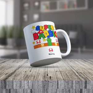 May include: White ceramic mug with a colorful Super Daddi design featuring a Mario-themed graphic with a mushroom, a question mark block, a pipe, and a star. The mug has the name Harry printed on the bottom.