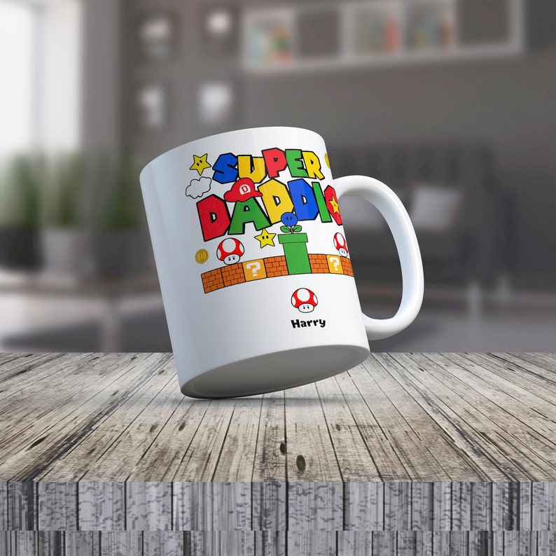 May include: White ceramic mug with a colorful Super Daddi design featuring a Mario-themed graphic with a mushroom, a question mark block, a pipe, and a star. The mug has the name Harry printed on the bottom.