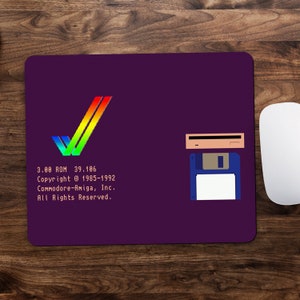 May include: A purple mouse mat featuring a rainbow coloured Amiga logo, a floppy disk, and a hard drive. The text on the mouse mat reads "3.00 ROM 39.186 Copyright @ 1985-1992 Commodore-Amiga, Inc. All Rights Reserved."
