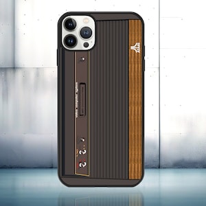 May include: A black phone case with a wood-grain design and a retro Atari video computer system graphic. The case has a white camera lens area with three lenses.