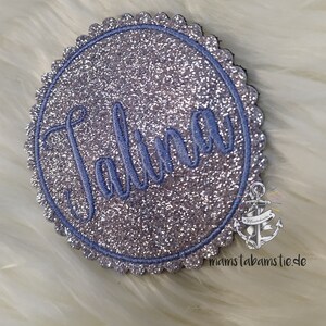 Könnte beinhalten: Ein silberner Glitzerkreis mit einem gewellten Rand und einem blauen gestickten Namen "Jalina".