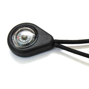 Puede incluir: Un llavero negro con una brújula y un cordón negro. La cara de la brújula tiene un fondo blanco con marcas negras y una aguja roja.