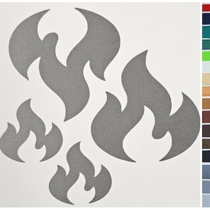 Pode incluir: Um conjunto de decalques cinzentos em forma de chama em vários tamanhos. Os decalques são cortados de um material texturizado e são dispostos sobre um fundo branco. As chamas têm um design estilizado e moderno, adequado para veículos ou decoração.