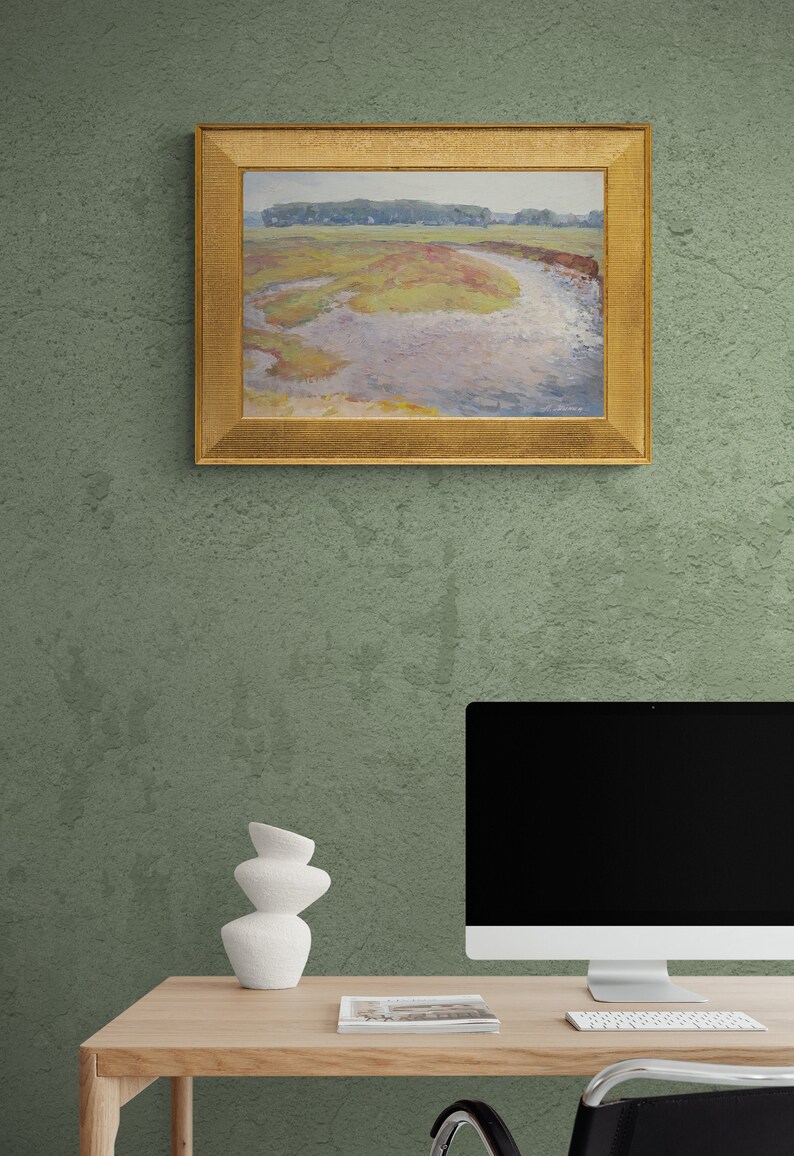 May include: A framed landscape painting depicting a river meandering through a field with green trees in the background. The painting is hung on a green wall above a desk with a computer, a white vase, and a magazine.
