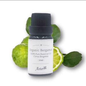 May include: A dark glass bottle of organic bergamot essential oil with a black cap, a white label, and green bergamot fruit and leaves. The label reads "Organic Bergamot 100% Pure Essential Oil Citrus bergamia -10ml-" and the brand name is Aster.