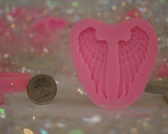 May include: Pink silicone mold shaped like a heart with two angel wings inside. The mold is about the size of a US quarter.