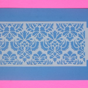May include: A blue stencil with a white damask pattern. The stencil has a cut-out circle on the right side.