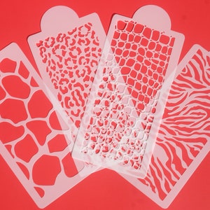 May include: Four white plastic stencils with different animal print designs: giraffe, leopard, crocodile, and zebra. The stencils are on a red background.