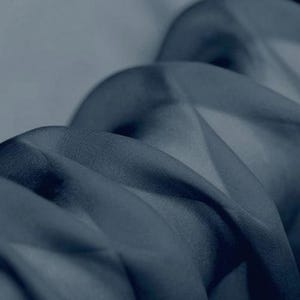 May include: Close-up of flowing, navy blue fabric. The material appears to be lightweight and sheer, with soft folds and subtle highlights. The fabric's texture is smooth, creating a sense of movement and depth.