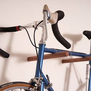 May include: A blue bicycle with a wooden wall mount. The bicycle has a black handlebar with black tape and a brown saddle.