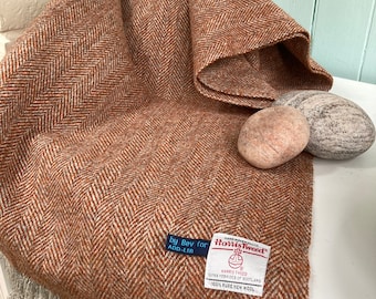 May include: A brown and white herringbone tweed scarf with a fringe border. The scarf has a label that reads "Harris Tweed" and "100% Pure New Wool".