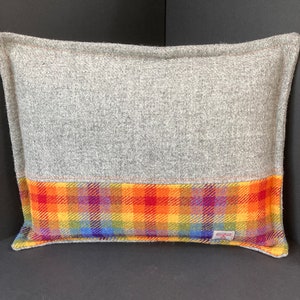 May include: Rectangular gray pillow with a vibrant plaid pattern in shades of red, orange, yellow, green, and blue. The pillow is made of a textured fabric, with a solid gray top and a colorful plaid bottom.