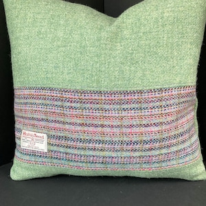 May include: Green and multi-colored striped pillow with a Harris Tweed label. The pillow is made of a soft, woven fabric.
