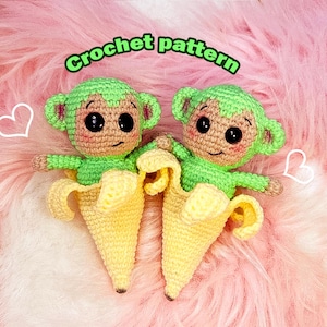 Pode incluir: Dois macacos de crochê feitos à mão em cascas de banana. Os macacos têm cabeças e braços verdes, rostos castanhos e olhos pretos grandes. As cascas de banana são amarelas. O fundo é rosa e branco com o texto "Crochet pattern".