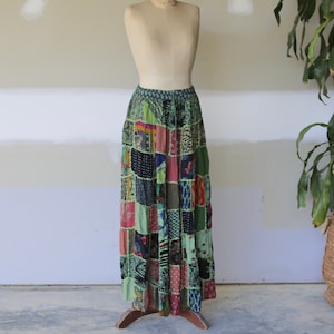 May include: A long, patchwork skirt with a green, blue, red, and black color scheme. The skirt is made of different fabrics and has a tiered design.