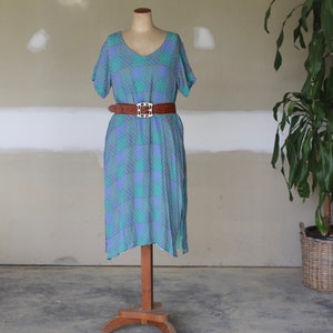 Puede incluir: Un vestido estampado azul y morado con un cinturón marrón en un maniquí. El vestido tiene mangas cortas y cuello en V.