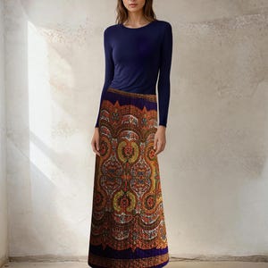 Può includere: Un top blu navy a maniche lunghe abbinato a una gonna lunga fantasia. La gonna presenta un design dettagliato e ornato nei toni dell'arancione, giallo e marrone, con un bordo blu scuro. Le scarpe da ginnastica bianche completano l'outfit.