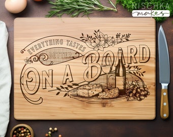 Peut inclure: Une planche à découper en bois avec le texte "Everything Tastes Better On A Board" gravé dessus. La planche présente une illustration stylisée d'une bouteille de vin, un verre de vin, du fromage et des raisins.