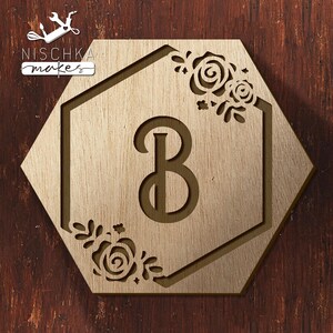 May include: A wooden hexagonal sign with a floral design and the letter "B" in the center. The sign is a light brown color and has a rustic look.