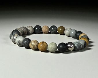 May include: A beaded bracelet featuring a variety of natural stone beads in shades of gray, black, brown, and beige. The bracelet includes a single, shiny, silver-colored bead. The beads are round and strung together to form a flexible bracelet.
