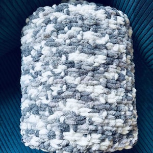 May include: A soft, fluffy, gray and white knitted throw pillow. The pillow is made with a chunky yarn and has a textured look.