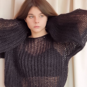 May include: A black, sheer, knitted sweater with a loose fit and long sleeves. The sweater is made of a soft, lightweight yarn and has a relaxed, casual style.