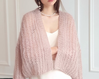 May include: A pale pink knitted cardigan with a loose fit and long sleeves. The cardigan is made of a soft, delicate yarn and has a slightly open front.
