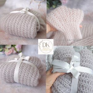 May include: A light gray knitted baby blanket with a white satin ribbon tied around it. The blanket is made of a soft, delicate yarn and has a delicate, lacy texture. The blanket is folded in half and tied with a white ribbon. The blanket is perfect for a newborn baby.