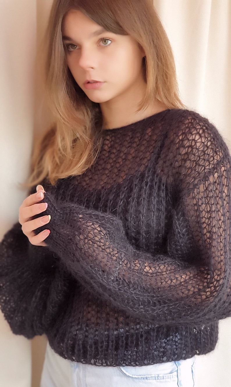 May include: A black, sheer, knitted sweater with a loose fit and long sleeves.