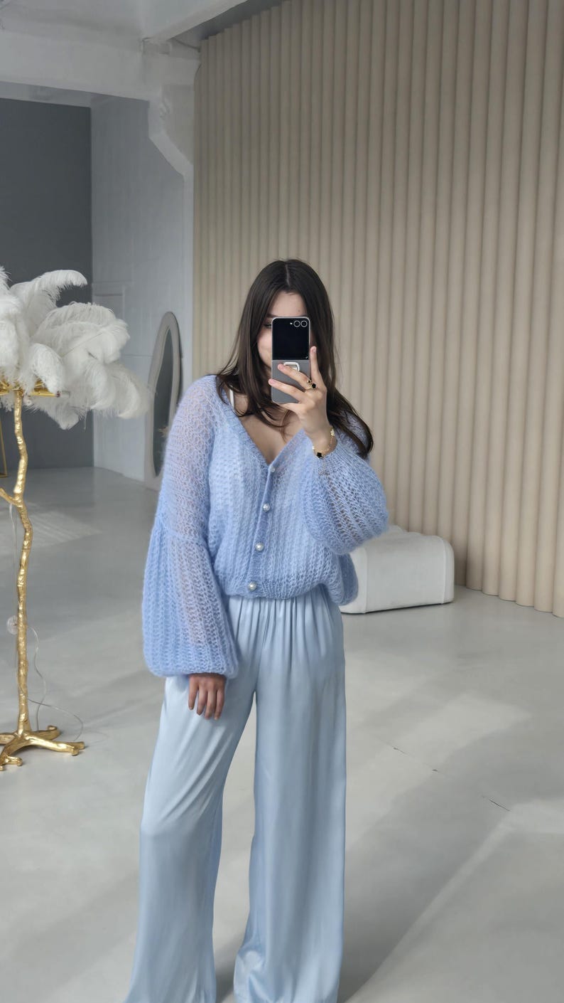 May include: A light blue knitted cardigan with pearl buttons and long, puffed sleeves. The cardigan is paired with matching light blue wide-leg pants.